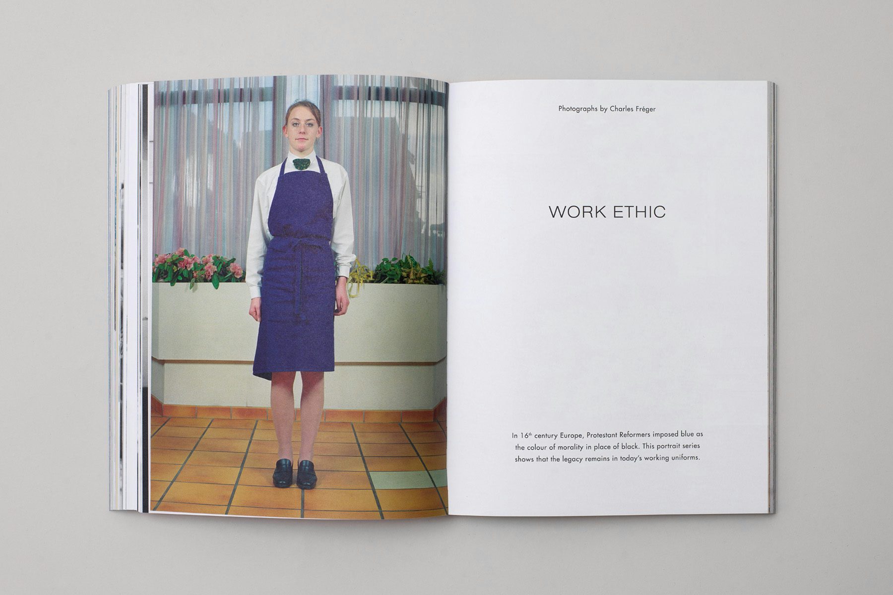 Photograph of a spread from the Blue issue of The Colour Journal, showing a full length photo of a person wearing a blue apron and a white shirt in front of two windows on the left hand page, and text on the right hand page headlined 'Work ethic'