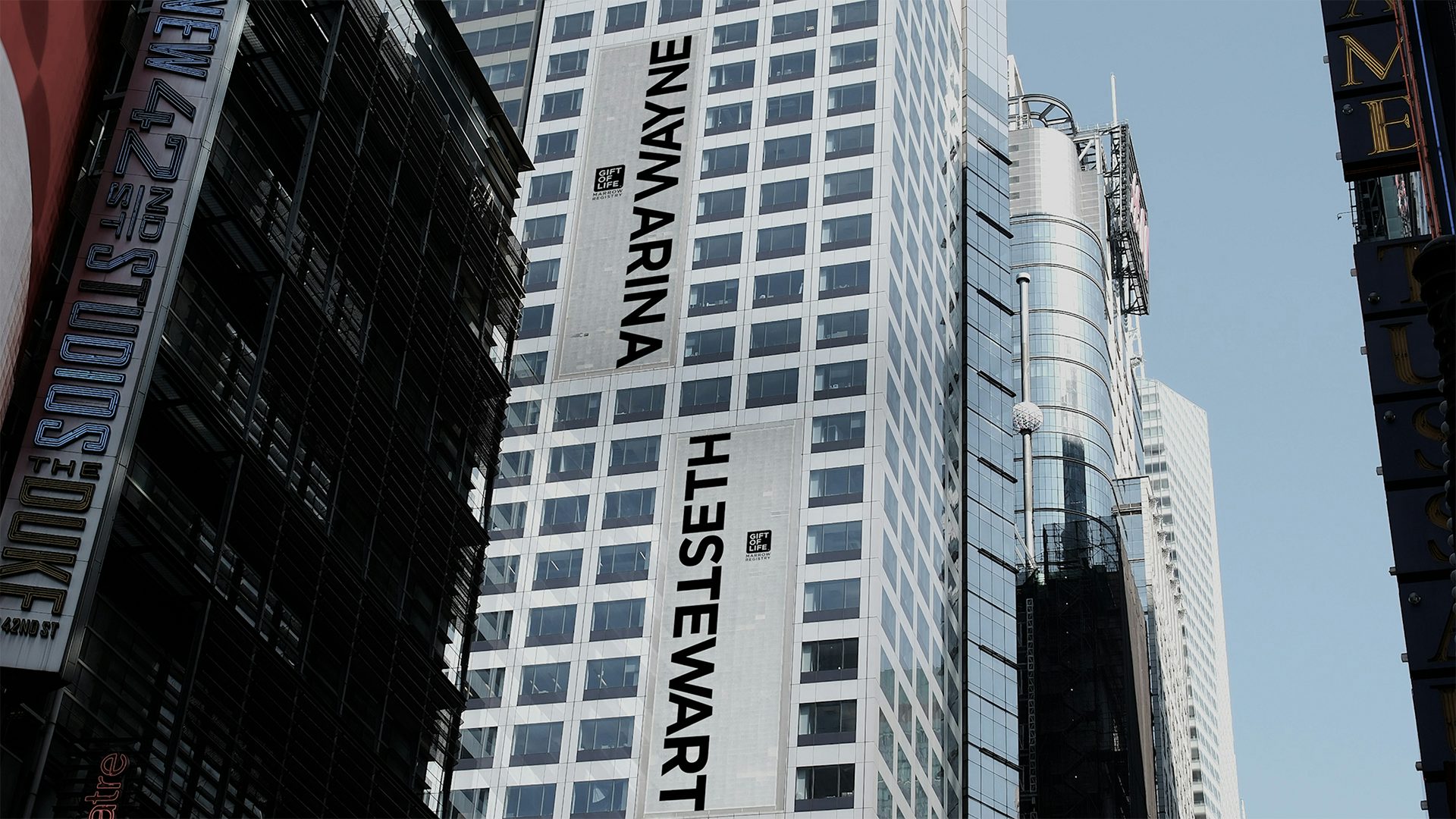 Photograph of large outdoor posters attached to a skyscraper, which feature the names Marina and Wayne, and Seth and Stewart