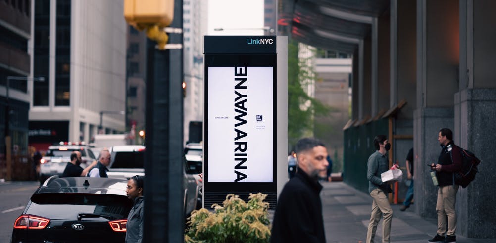 Photograph of a digital outdoor display in a city street, featuring the names Marina and Wayne joined by the letters 'M' and 'W'