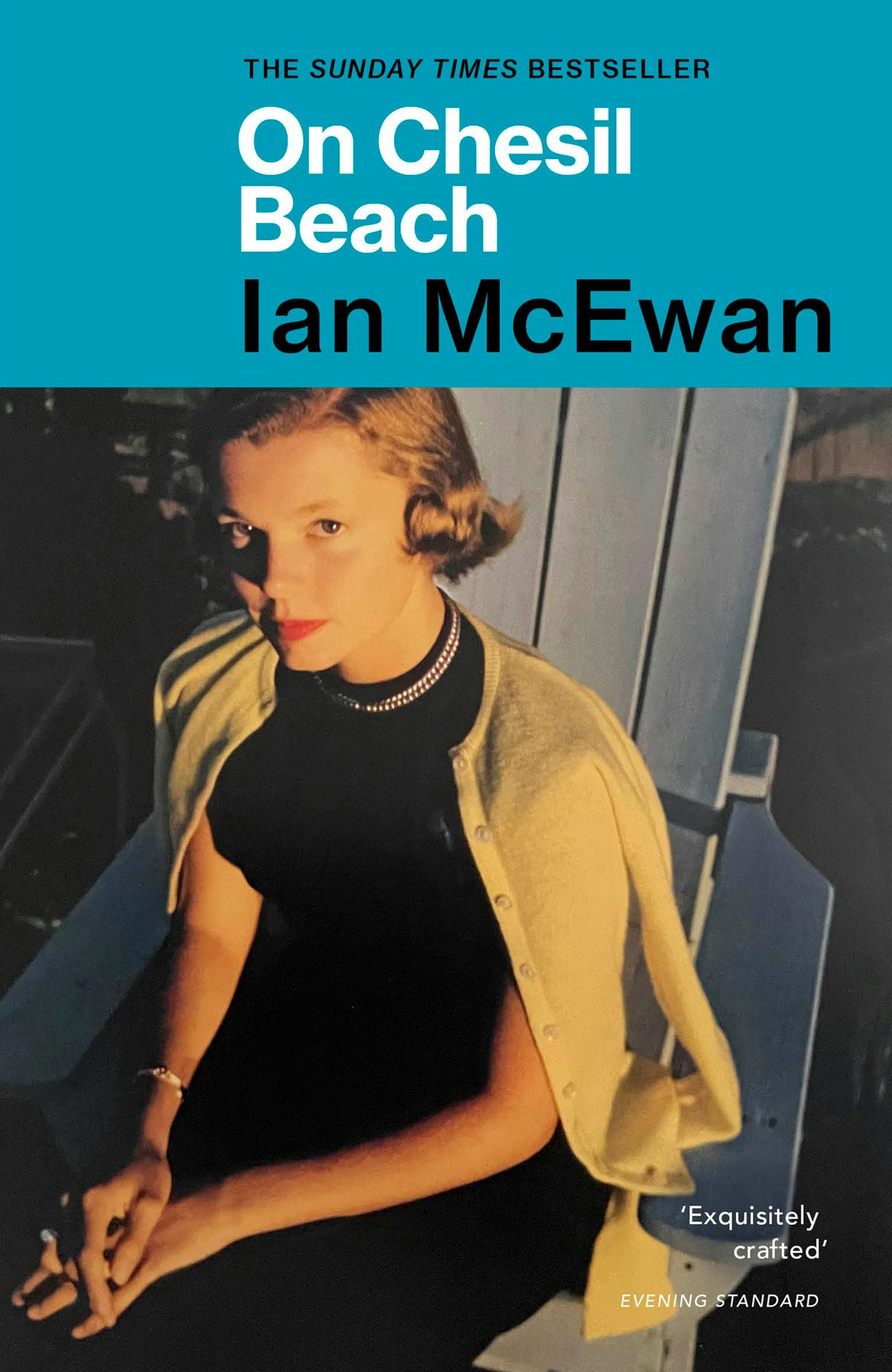 Cover of On Chesil Beach by Ian McEwan showing a warm hued photo of a young person with curled hair styled in a 1940s hairdo, wearing a beige cardigan over their shoulders, and their hands placed on top of each other on the person's lap