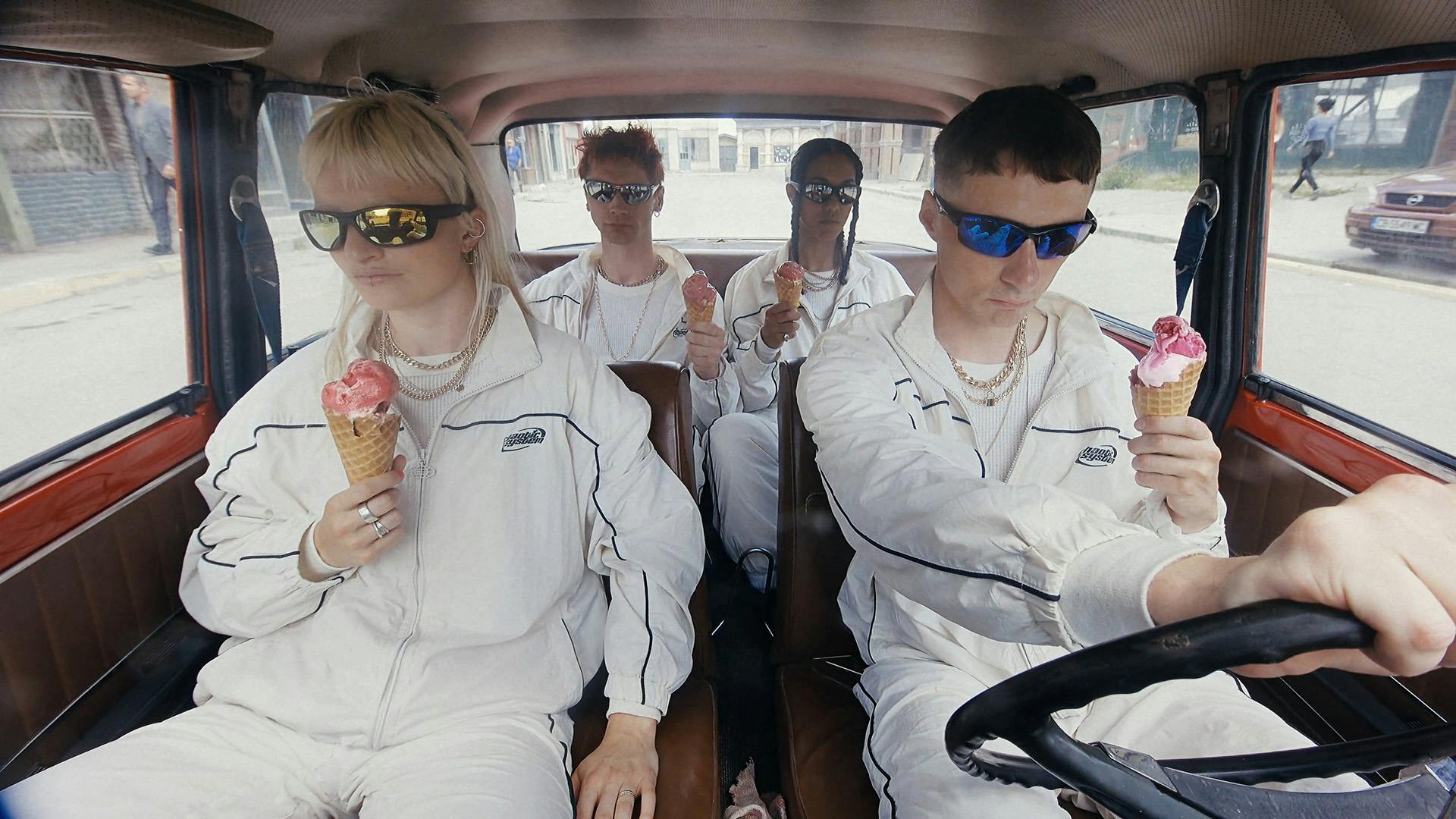 Still from Oscar Hudson's music video for Big Hammer by James Blake showing four young people in white matching tracksuits and visor sunglasses in a car, each holding an ice cream