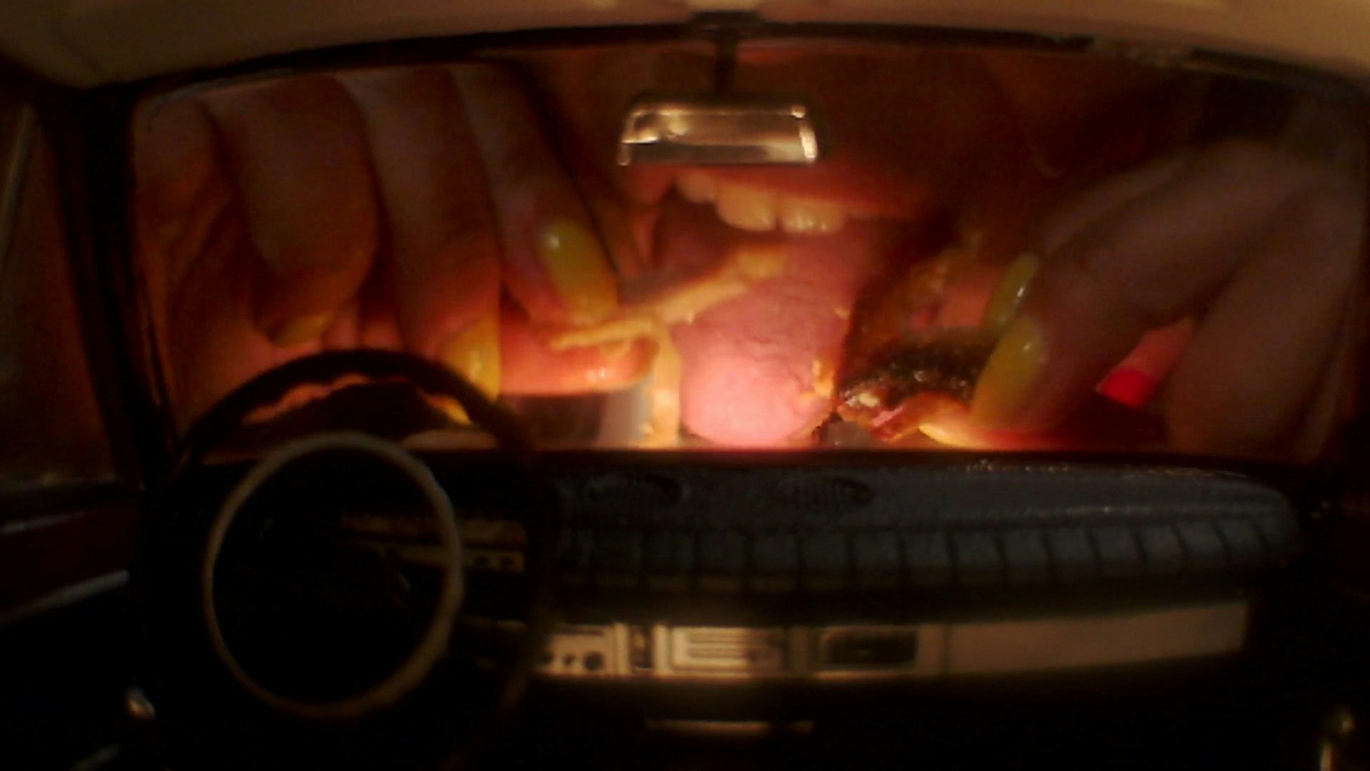 Still from Oscar Hudson's music video for Big Hammer by James Blake showing a large mouth appearing to lick food as seen through a car windscreen