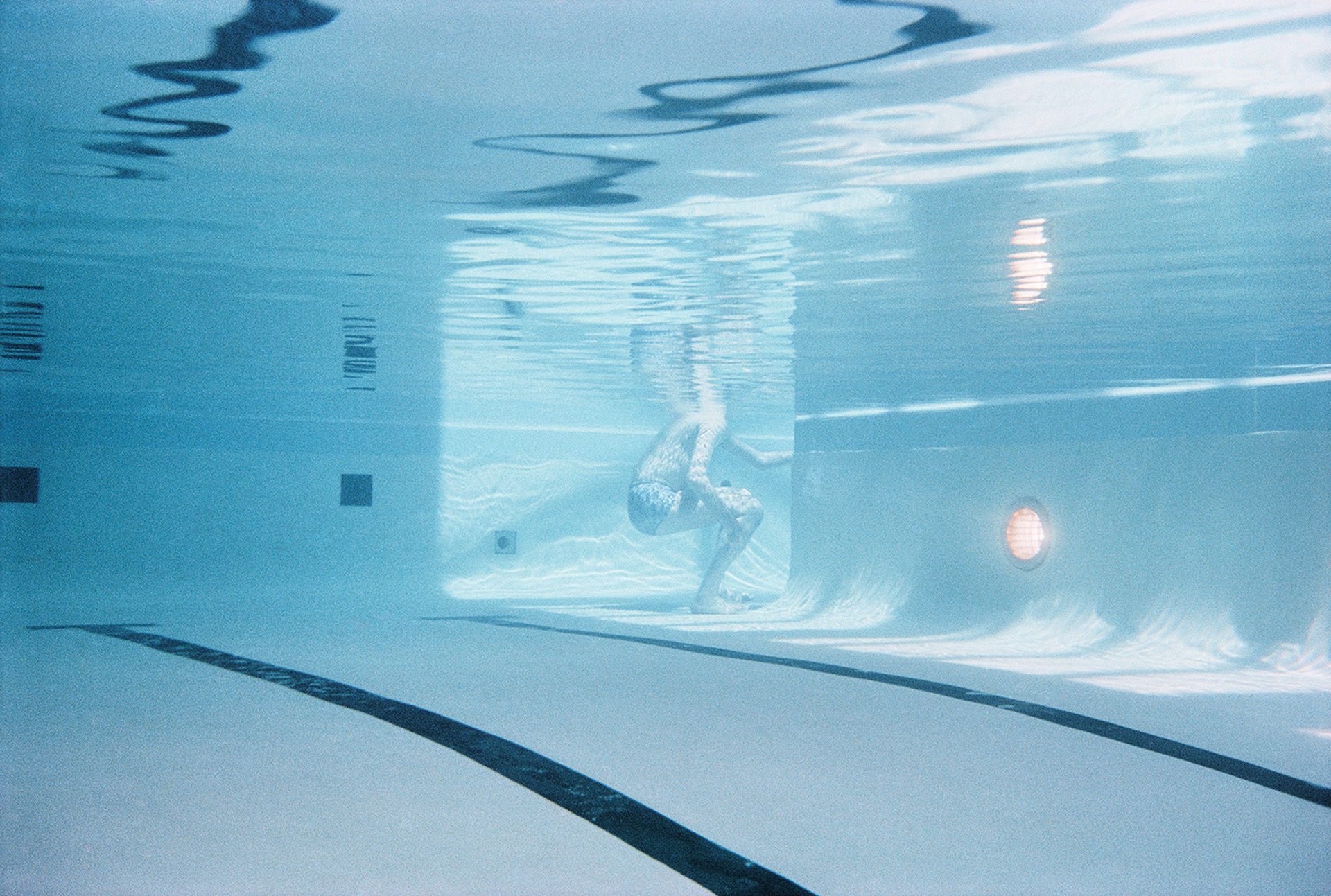 Photograph by Larry Sultan from his series Swimmers showing a person crouching down in a swimming pool touching the floor with their feet
