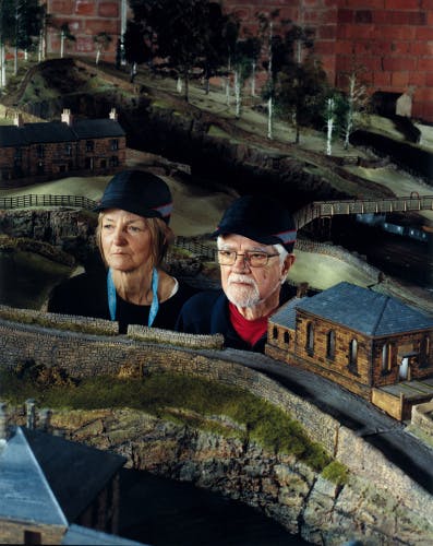Oliver Chanarin A Perfect Sentence showing two people wearing dark caps, with their heads jutting out from a model train setup