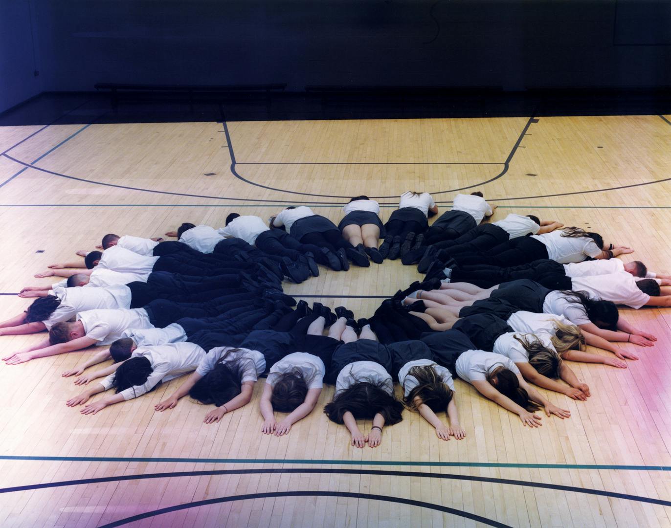 Oliver Chanarin A Perfect Sentence showing a group of school children lying on their front forming the shape of a circle on an indoor basketball court