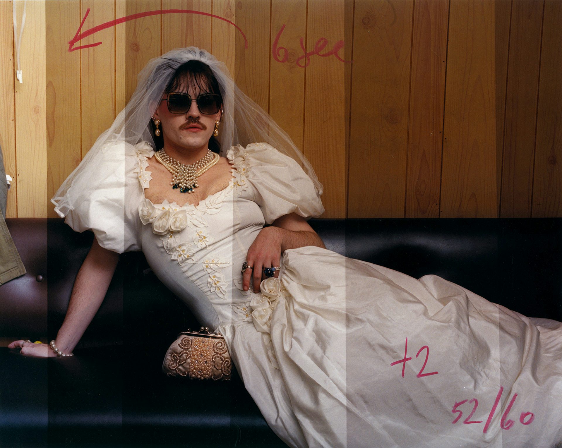 Oliver Chanarin A Perfect Sentence showing a person with a moustache and sunglasses and wearing a wedding dress and veil on a black sofa. The image is covered in red handwritten mark-ups, and has different brightness levels like a strip test