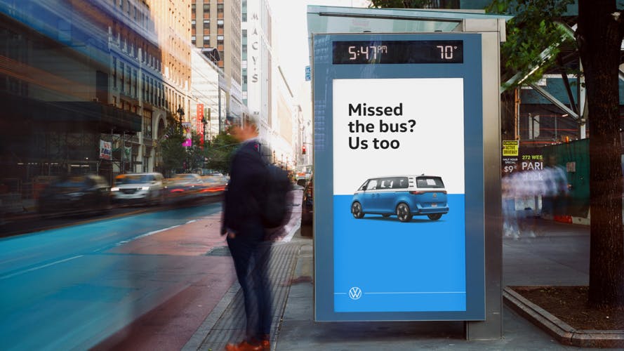 Photo of a vertical VW ID Buzz poster in a busy city street, with the tagline 'Missed the bus? Us too' above a two-tone blue and white VW bus against a matching blue and white background