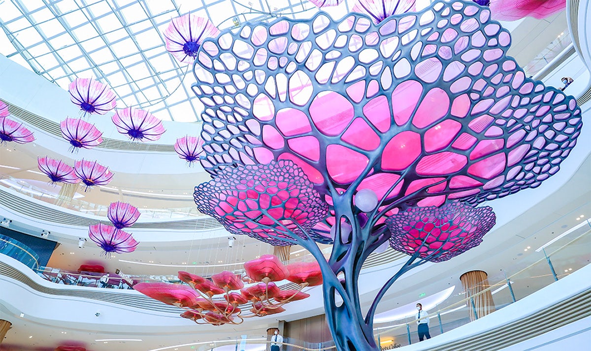 Image shows a large tree-like installation in pink and blue inside a Haikou shopping complex
