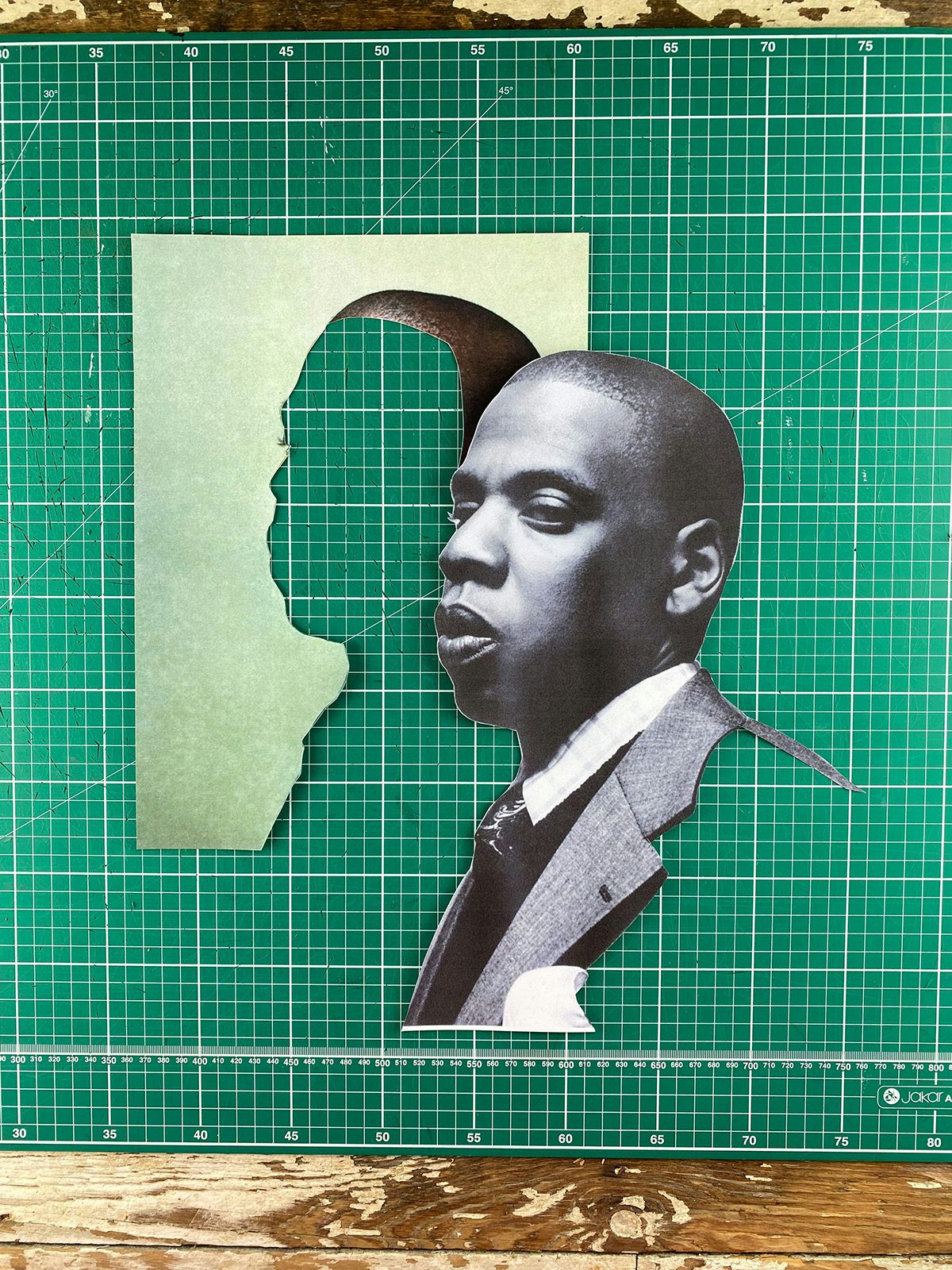 Image shows a black and white portrait photo of Jay Z cut out from its background, shown on a green cutting mat