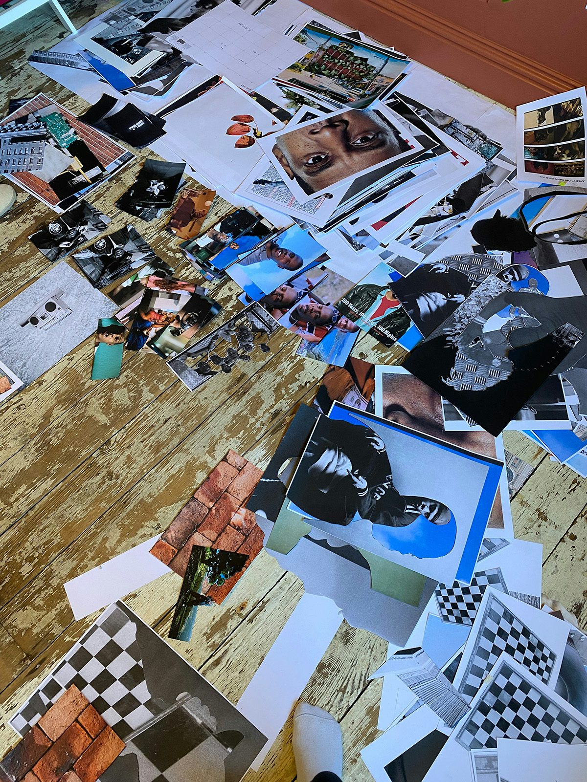 Image shows lots of photographs pertaining to Jay Z scattered on a wooden floor by artist Jazz Grant