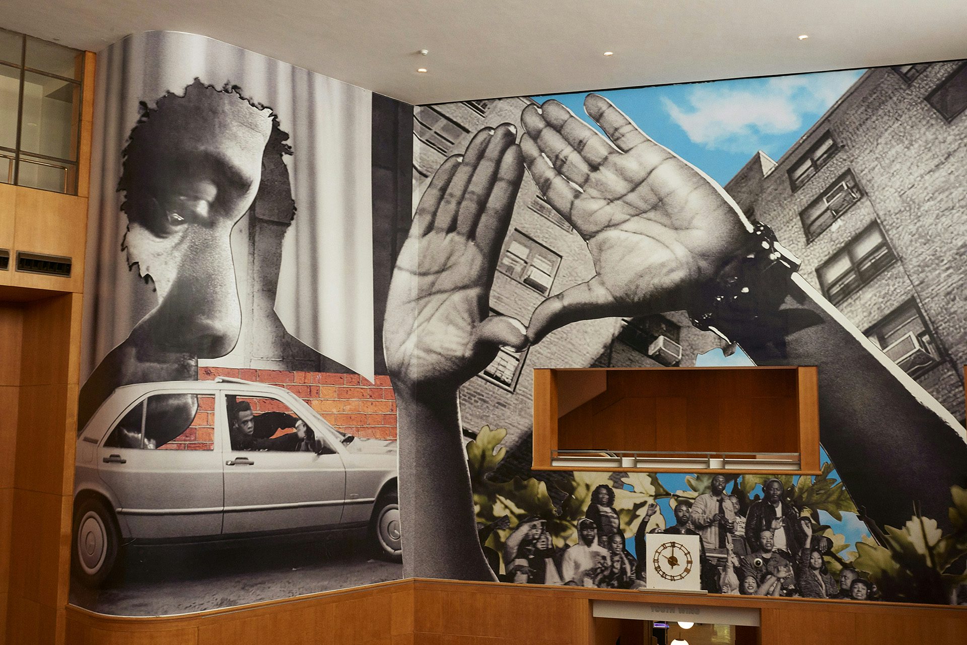 Photo of the main hall at the Brooklyn Public Library showing Jazz Grant's mural of Jay Z, including a cut-out of hands forming a shape of a triangle, a black and white portrait of the rapper, and a silver car