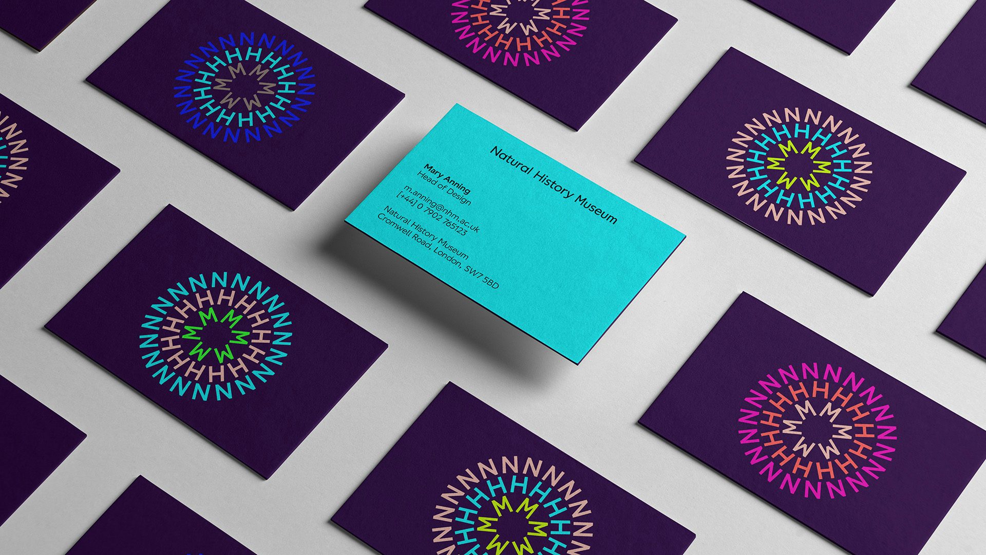 Image shows the new Natural History Museum branding on rows of purple business cards with the initials 'NHM' arranged in concentric circles, with one business card turned upside down to reveal a bright blue reverse side