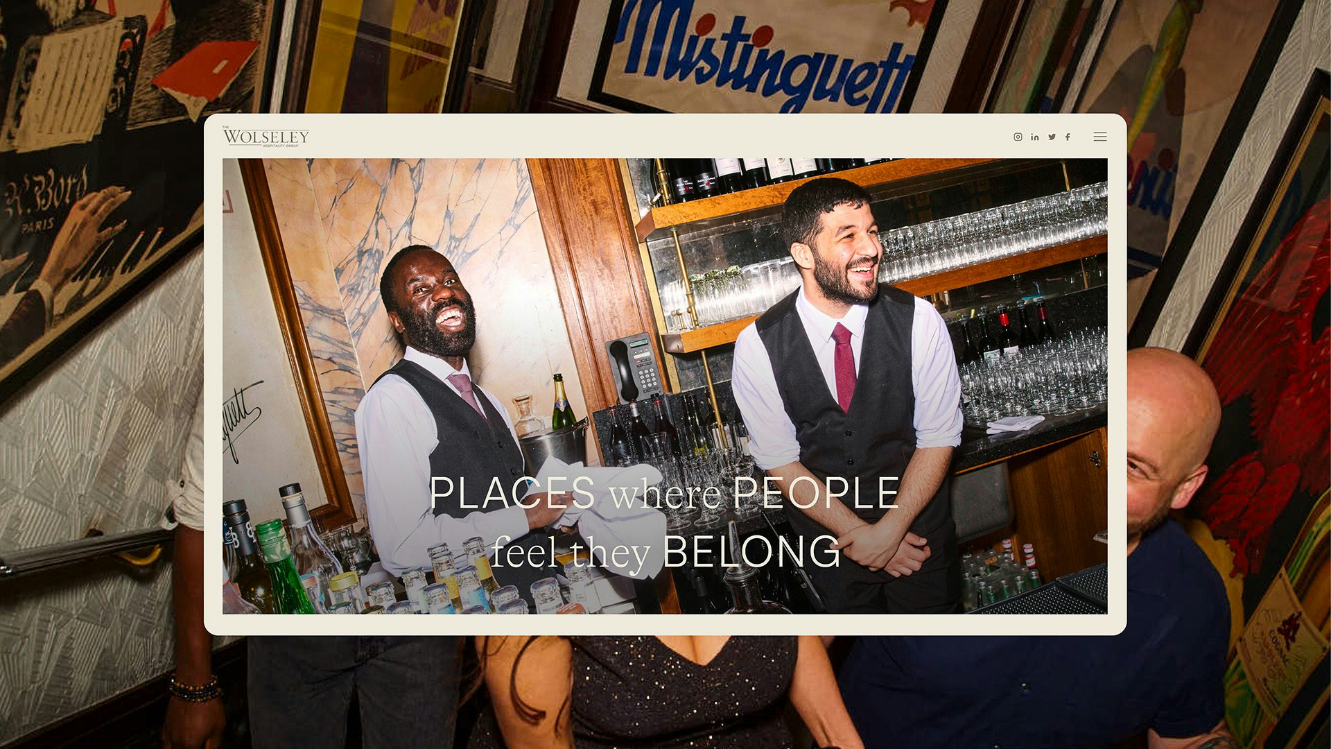 Photo of two bar staff in white shirts and black waistcoats stood smiling behind a bar filled with rows of glasses and bottles, as shown on a website screengrab from the Wolseley's new digital identity