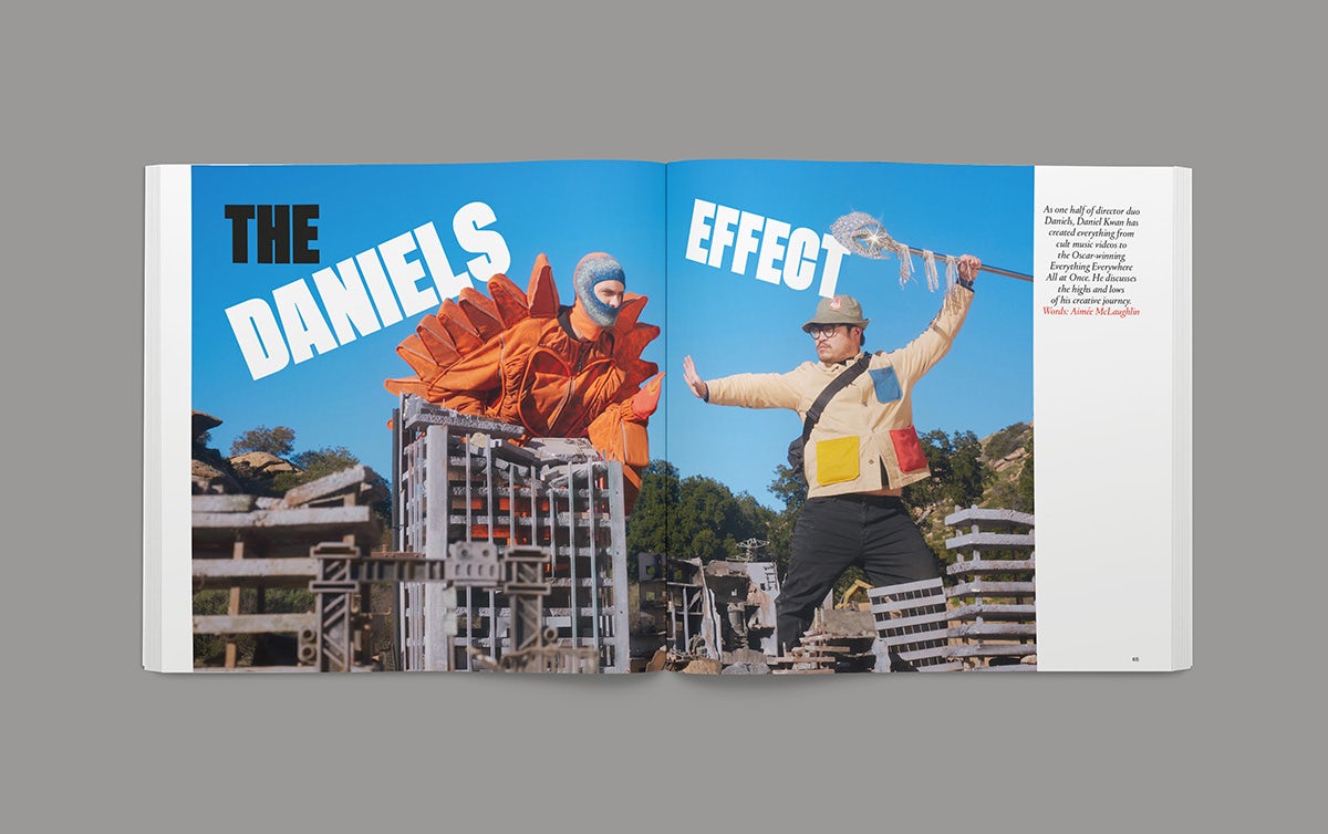 Image shows a spread from the Creative Review Creative Leaders 2023 issue, headlined 'The Daniels Effect' in thick capitals arranged at angles over the top of an image of two people looming above a small cityscape. One wears an orange dinosaur costume, the other wears an explorer-style outfit holding a spear above their head
