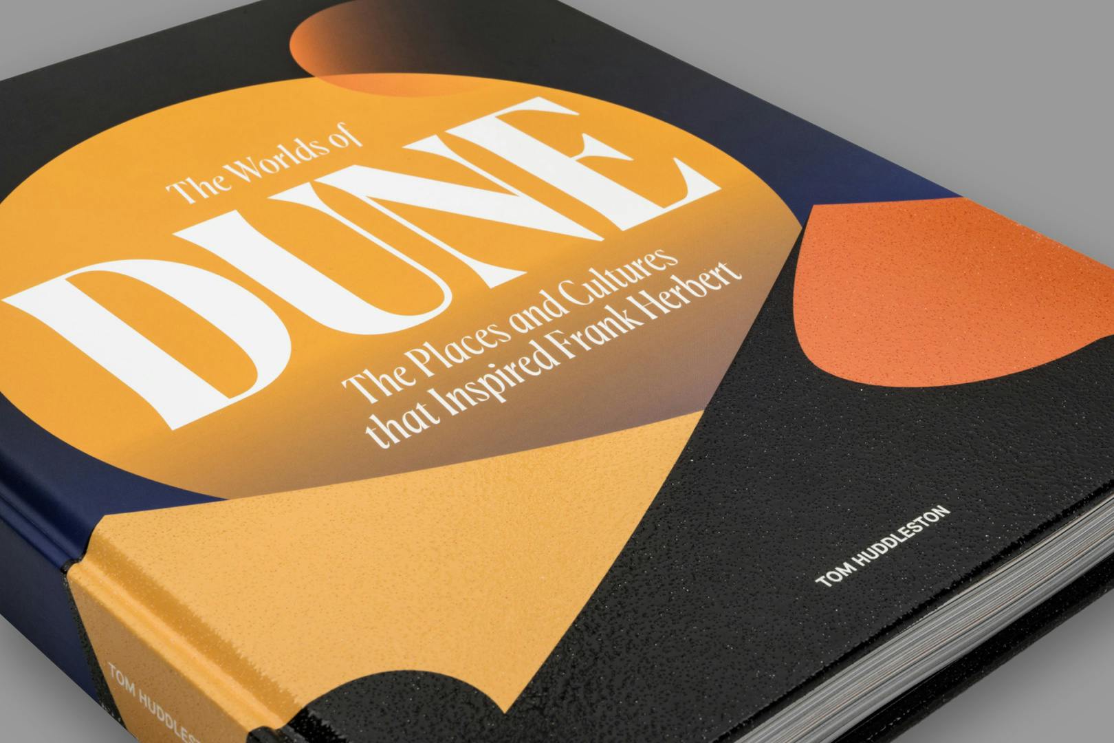 Close-up image of the front cover of a book about Dune, featuring minimal illustrations representing sand dunes, and a large planet-like circle looming over the top