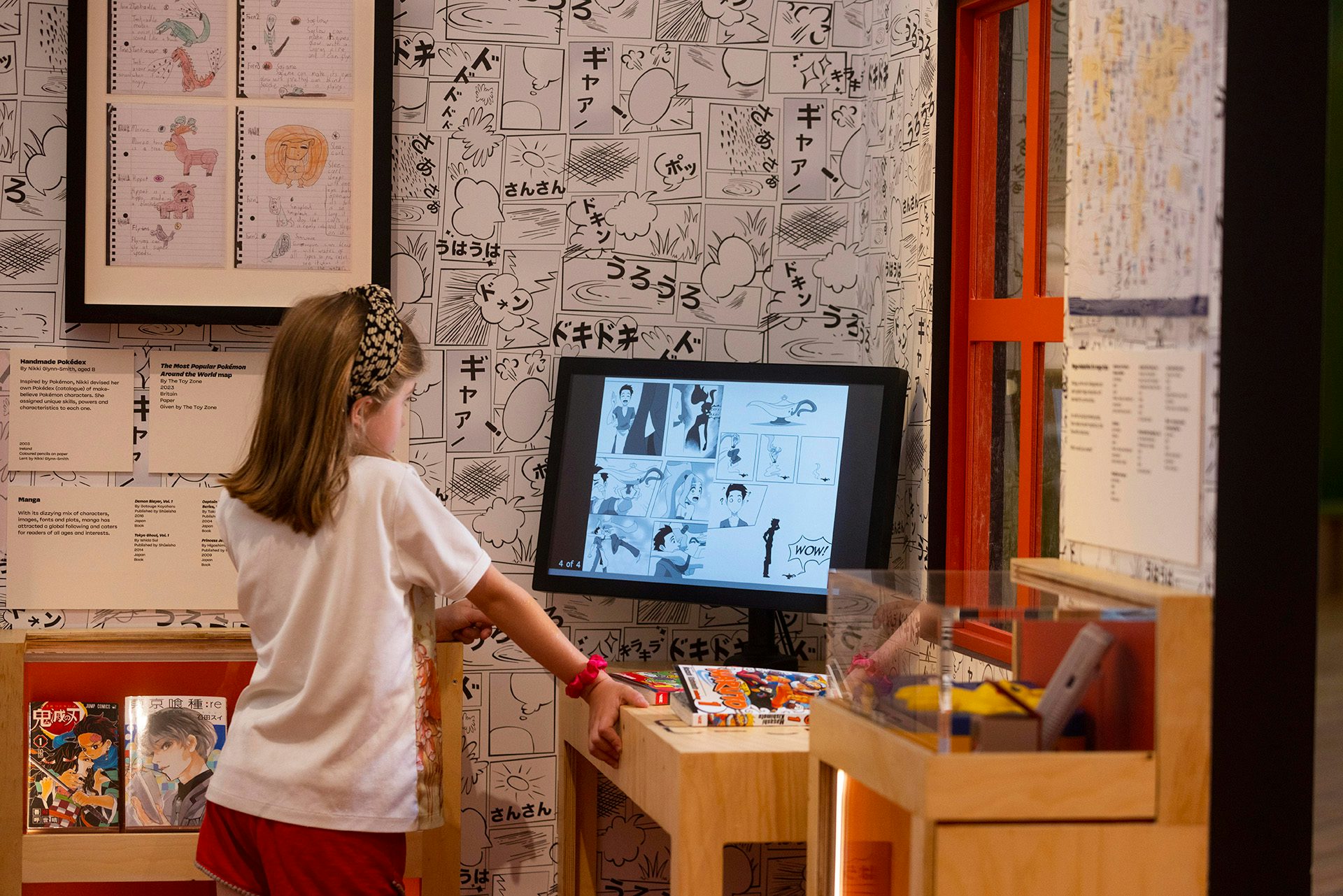 Photo of a child looking at a screen displaying manga inside a room decorated with black and white manga illustrations at the exhibition Japan: From Myths to Manga at the Young V&A