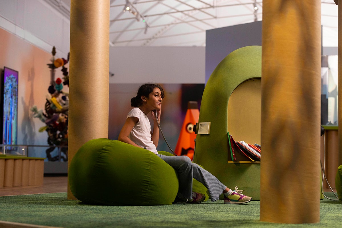 Photo of a young person sat on a green spherical seat listening to a device at the exhibition Japan: From Myths to Manga at the Young V&A