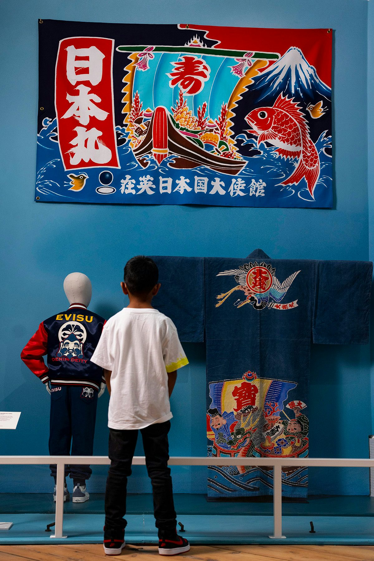 Photo of a child looking at a display including a Japanese wall hanging, a garment, and a bomber jacket at the exhibition Japan: From Myths to Manga at the Young V&A