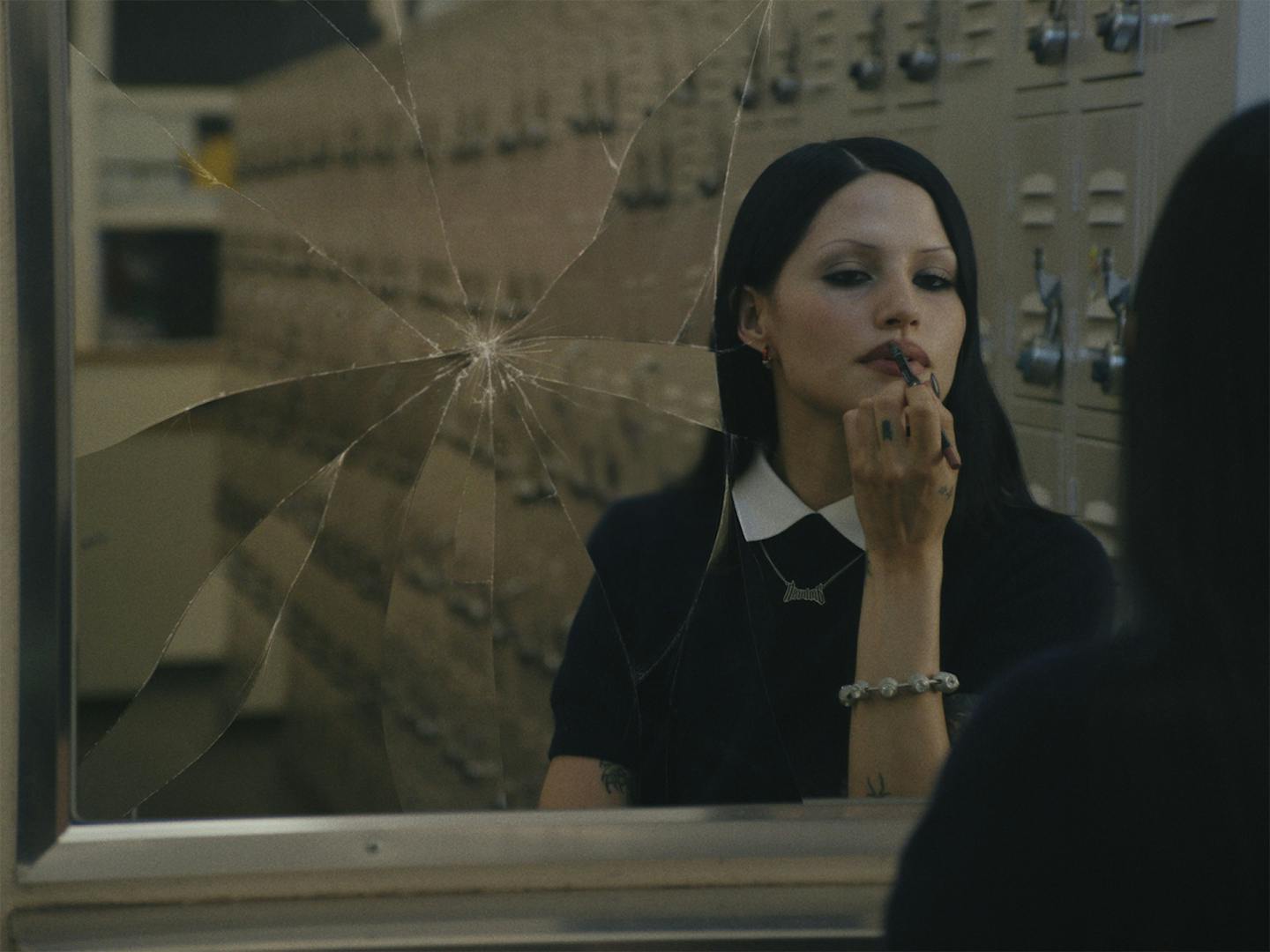 Still from Nike and Ambush commercial directed by Aidan Zamiri showing the campaign star with black hair, black dress and applying black lipstick in a cracked mirror