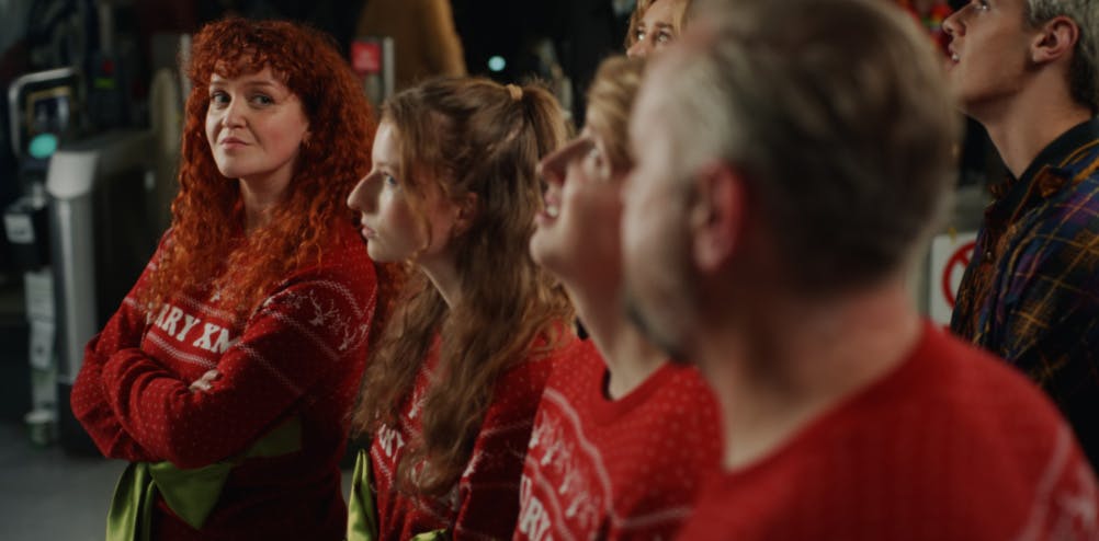 Still from McDonalds Christmas 2023 ad showing people wearing Christmas jumpers stood in a line