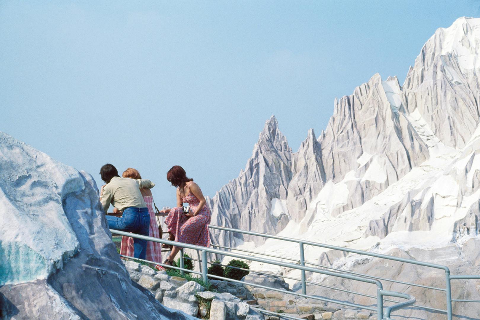 Photograph by Luigi Ghirri showing people walking up stairs in front of a replica model of the Alps