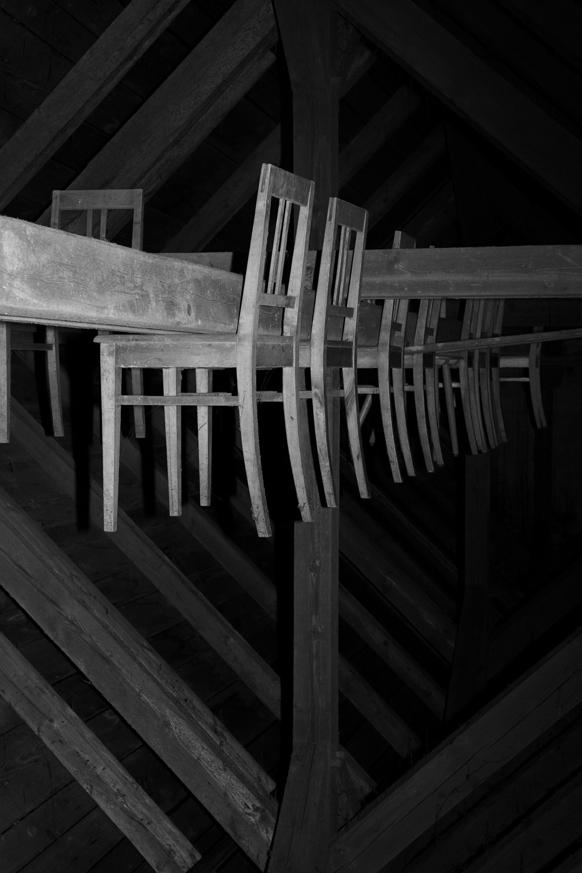 Black and white photograph from Plexus by Elena Helfrecht showing rows of chairs attached to wooden beams which appear to float in the air