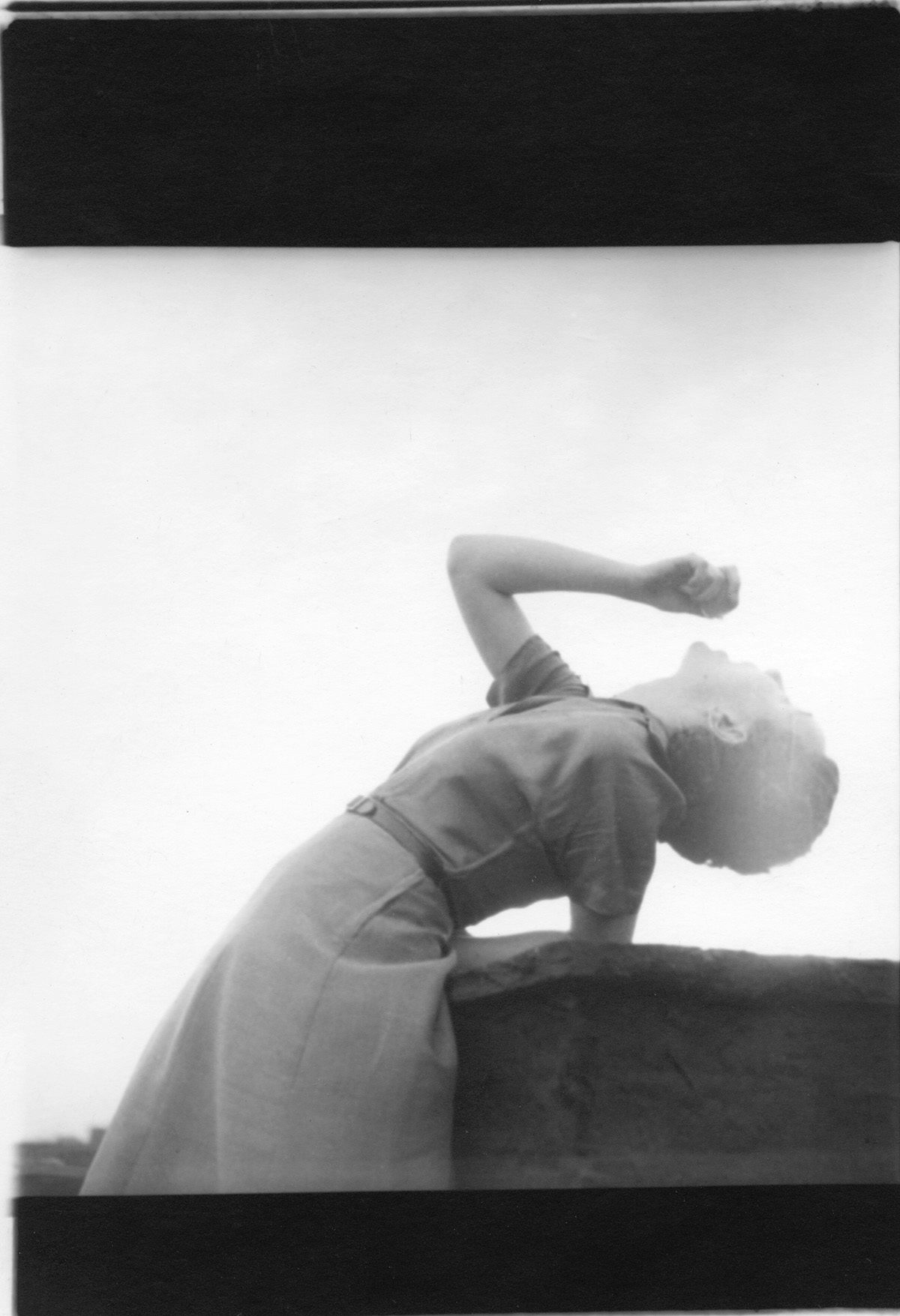 Black and white photograph by Saul Leiter showing a person with short hair wearing a dress and bending over backwards leaning up to the sky