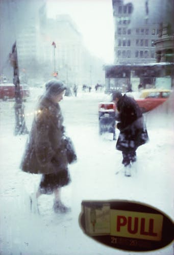 Photograph by Saul Leiter showing two people standing in a snowy city street seen through a damp window