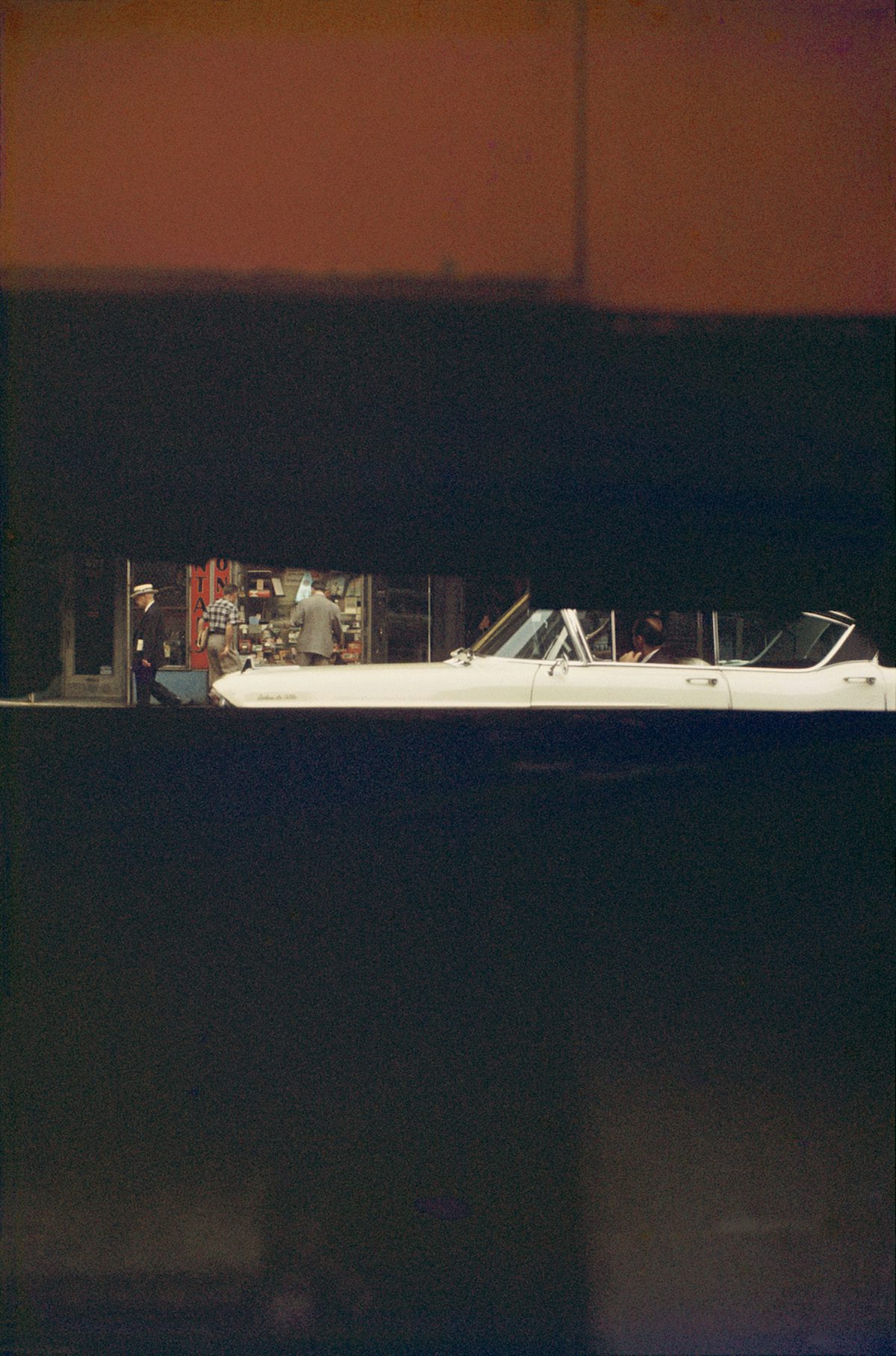 Photograph by Saul Leiter showing a sliver of a city street visible through a horizontal gap in a structure
