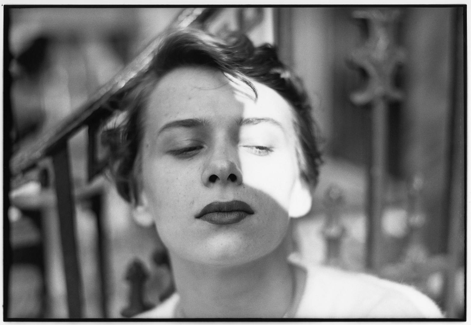 Black and white photograph by Saul Leiter of a woman with short hair glancing to the side with half of her face lit up and the other half in shadow