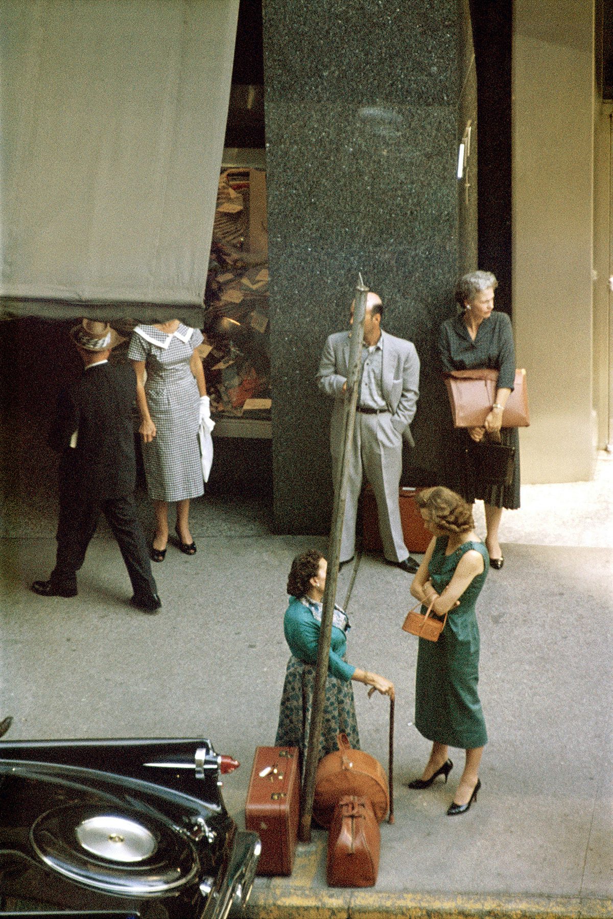 Photograph by Saul Leiter of two women standing next to luggage cases on a pavement