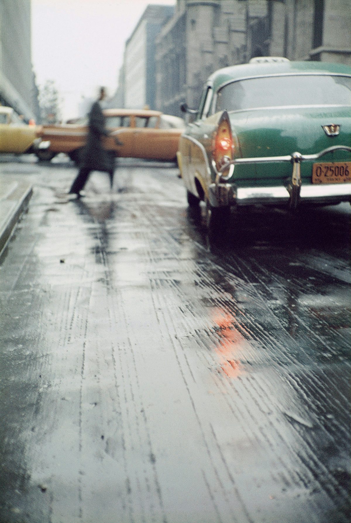 Photograph by Saul Leiter of a rainy city street with a blurred figure crossing the road in front of a green car