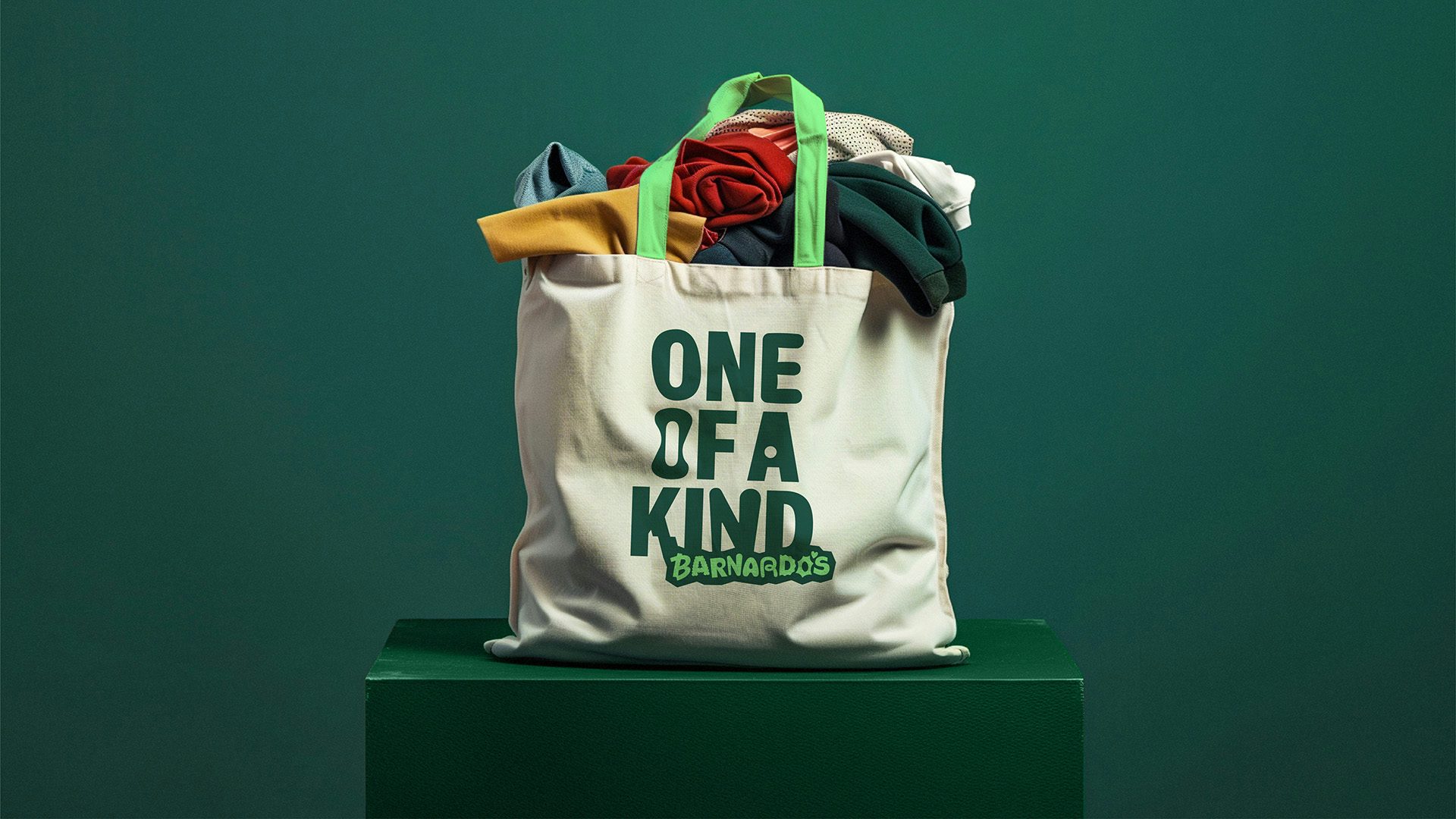 Image shows the new Barnardo's visual identity on a beige tote bag filled with clothing, featuring the slogan 'one of a kind'