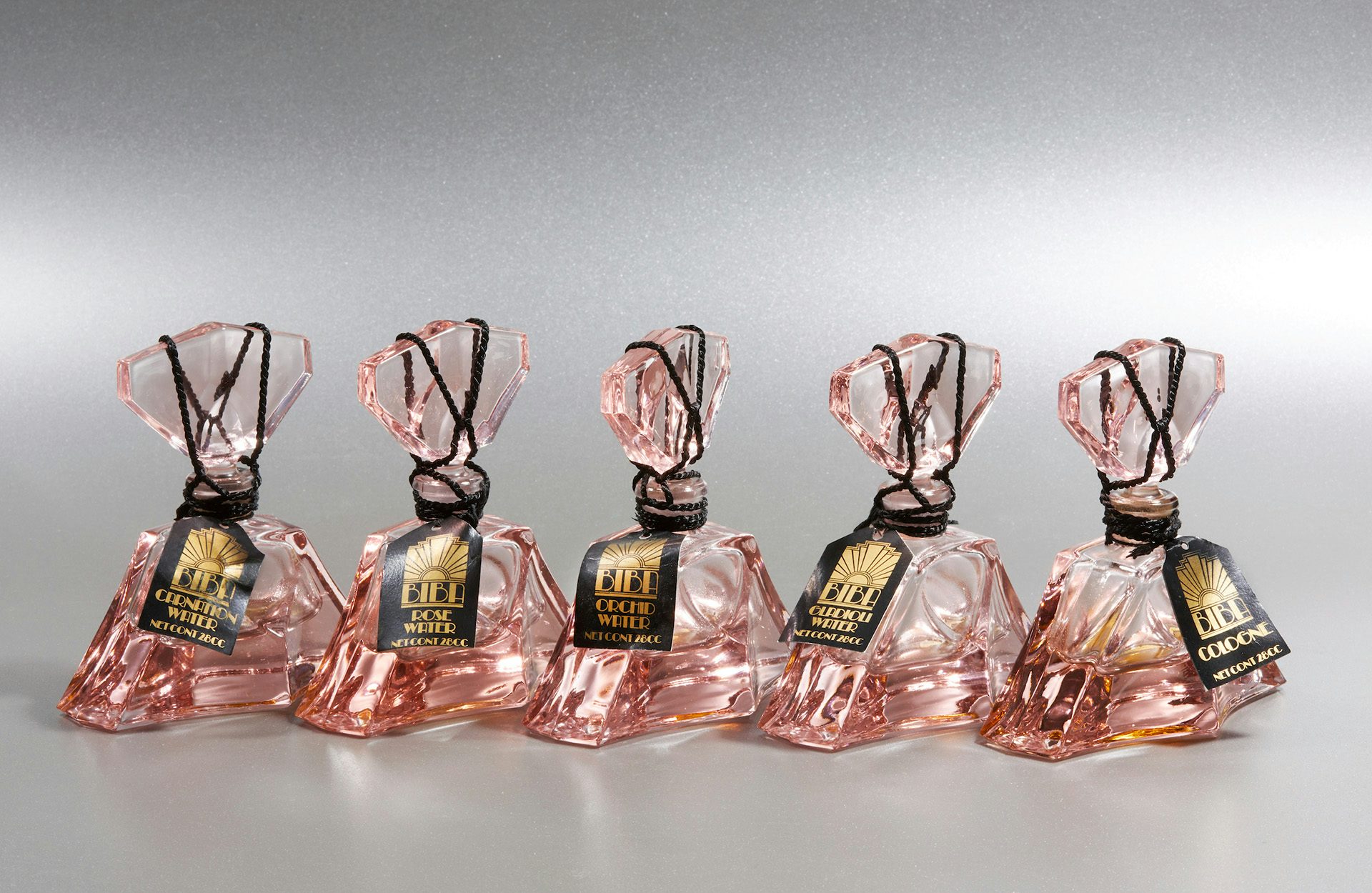 Photograph showing a row of five pink glass fragrance bottles by Biba