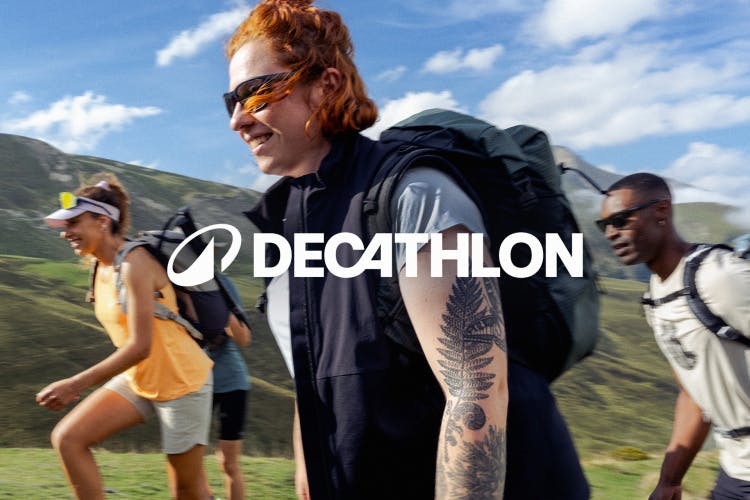Image shows Decathlon's new art direction style created as part of its new branding, as featured on a photo of people hiking in the sunny countryside with the new wordmark and circular logo laid over the top