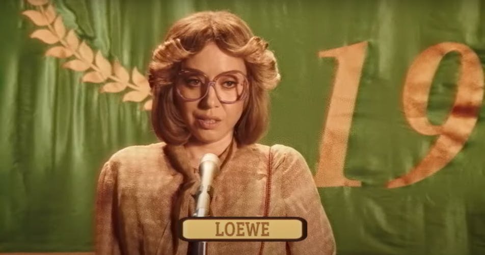 Still from a Loewe brand film showing Aubrey Plaza in a 70s outfit and hair style standing in front of a microphone