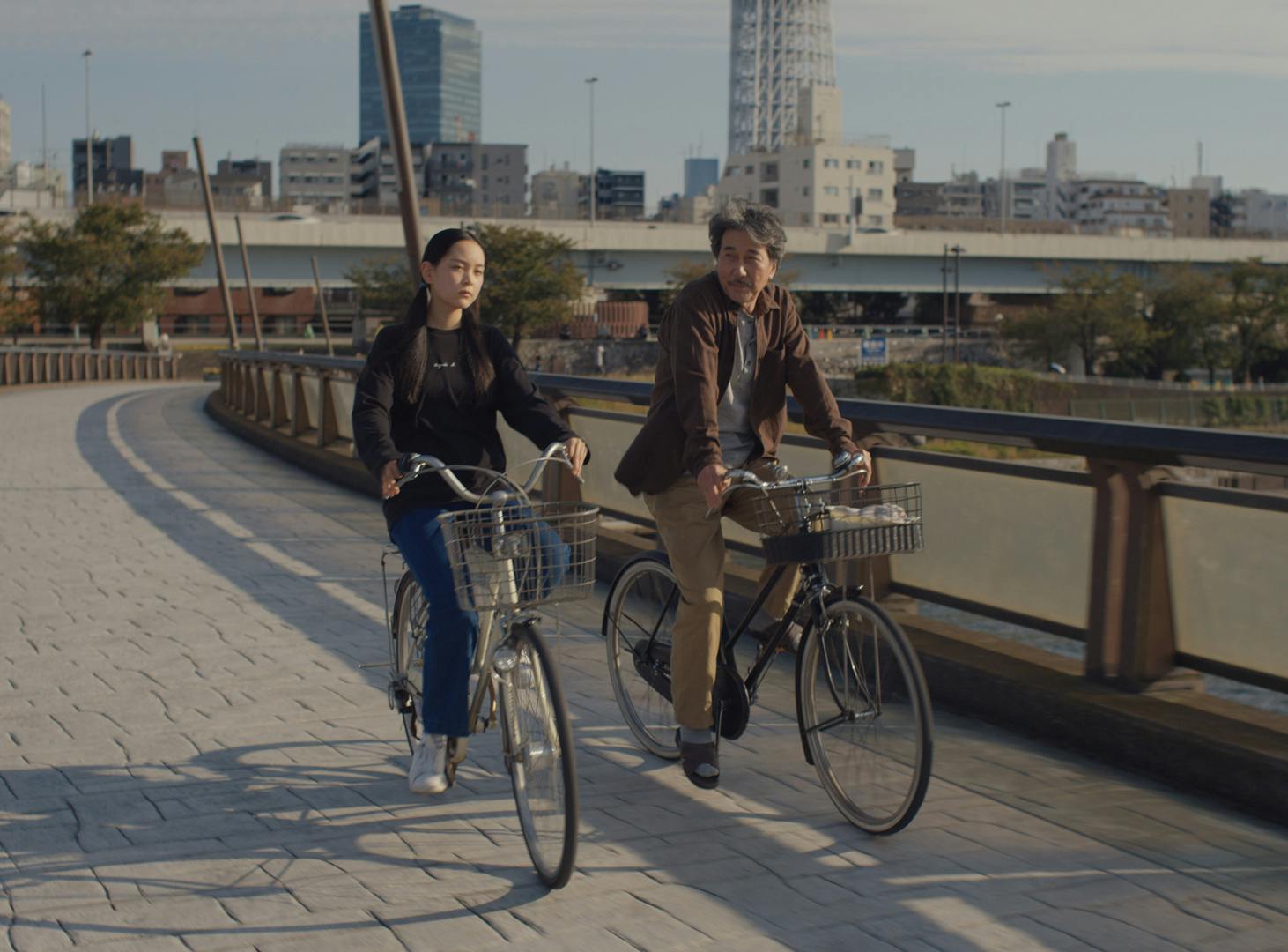Film still from Perfect Days showing main character Hirayama and his niece riding bikes over a bridge