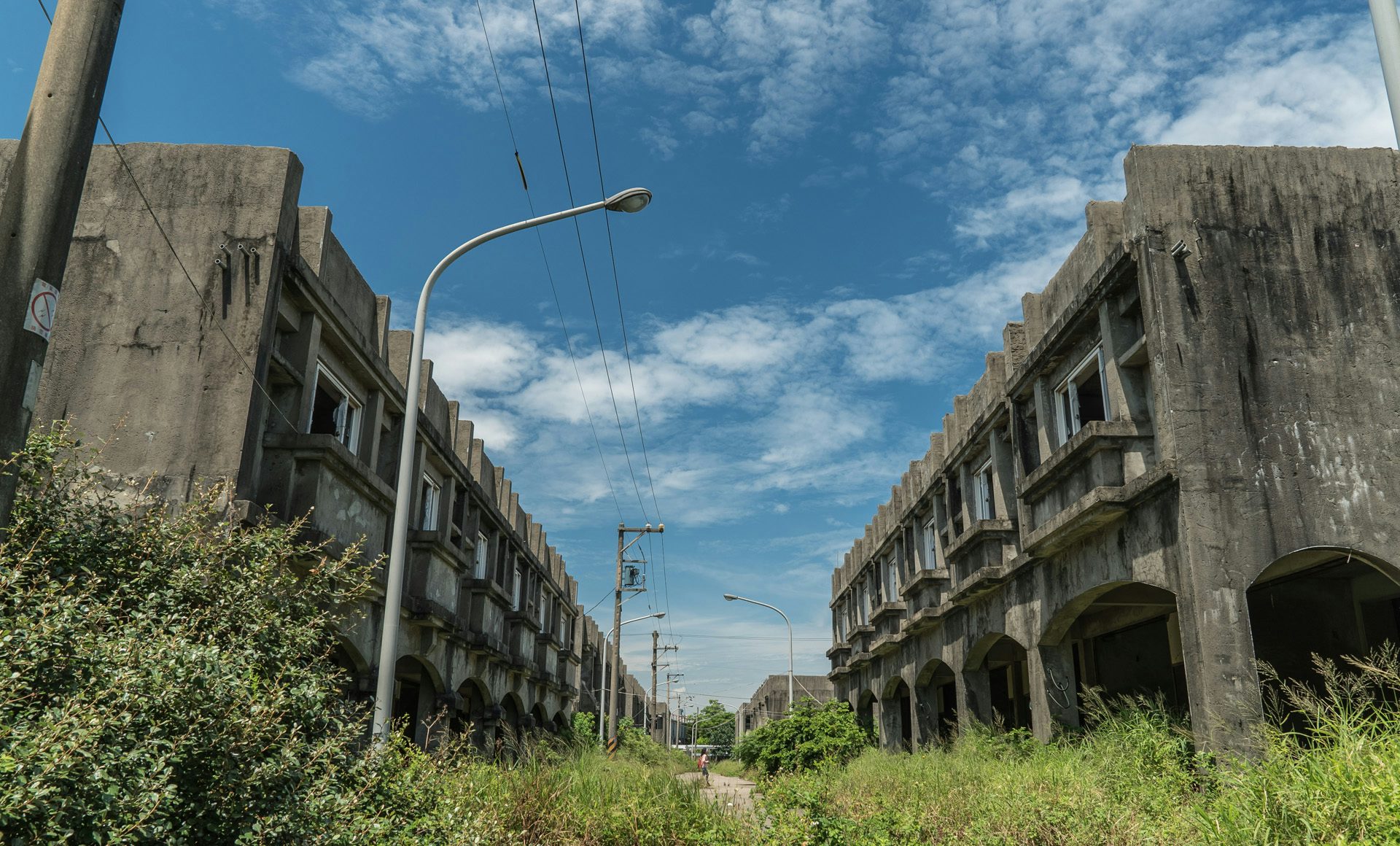 Photo from Project Urbex by Ikumi Nakamura showing two run-down buildings in an overgrown street
