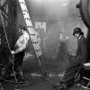 Black and white photograph from Vulcan's Forge showing people wearing workwear standing in a steam-filled room next to equipment and a ladder
