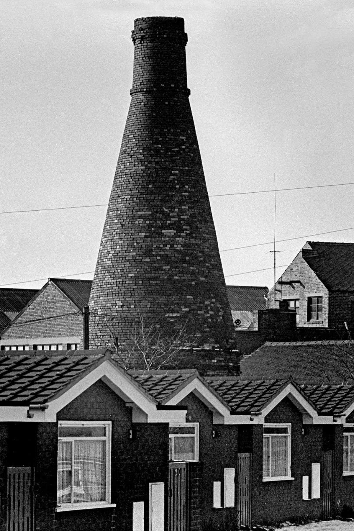 Vertical black and white photograph from Vulcan's Forge showing single-storey buildings surrounding a tall work building jutting out between them