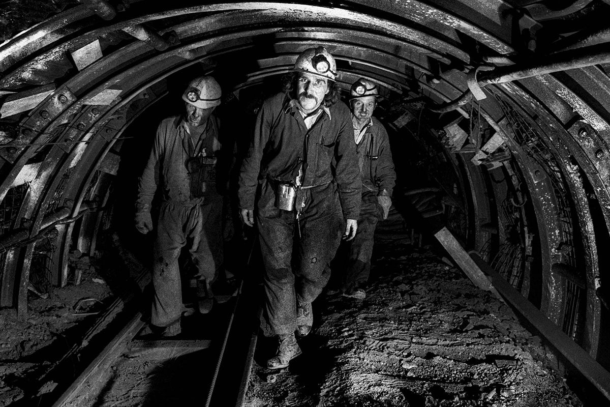 Black and white photograph from Vulcan's Forge showing three people wearing boiler suits and hard hats walking through an arched tunnel