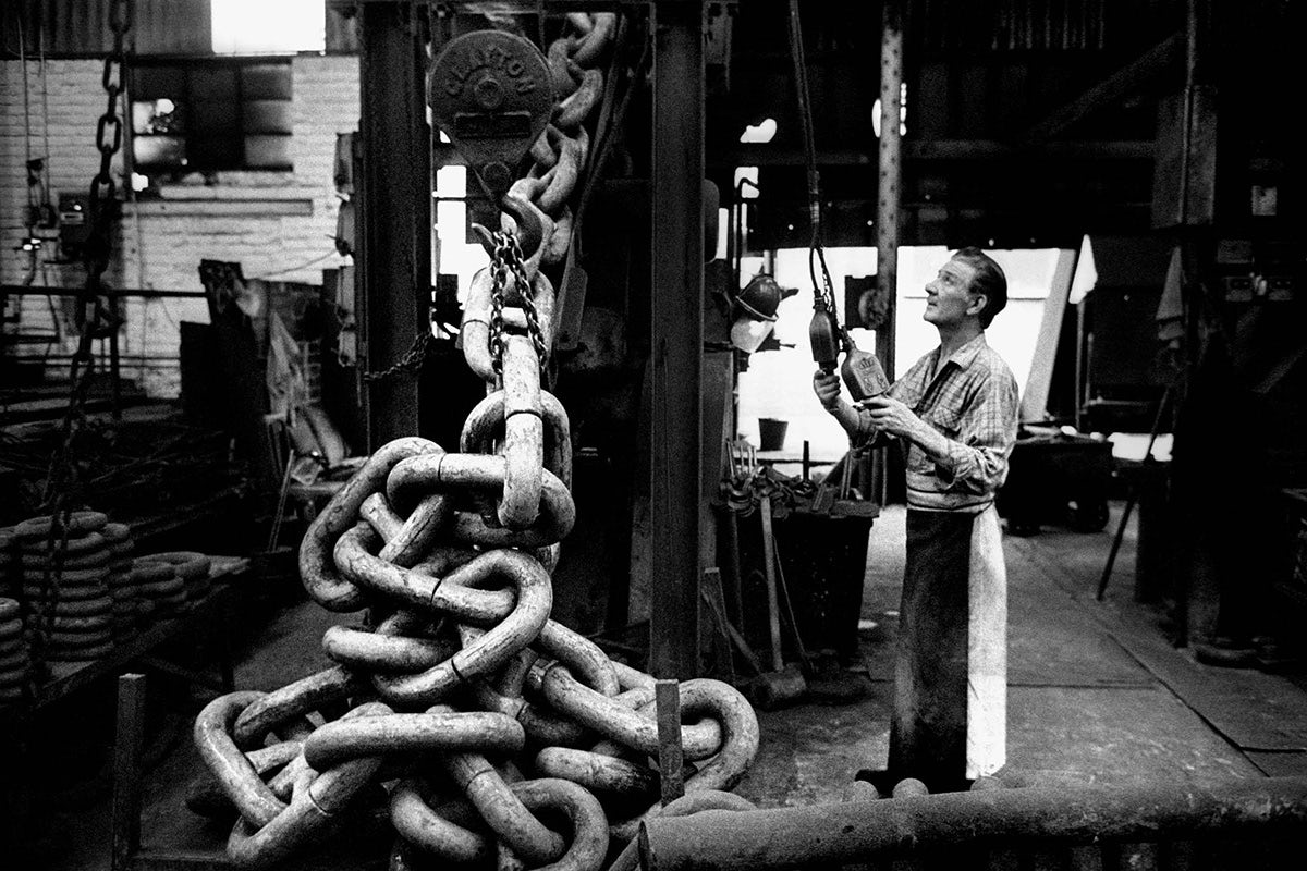 Black and white photograph from Vulcan's Forge showing a person holding equipment standing in front of a pile of large chains