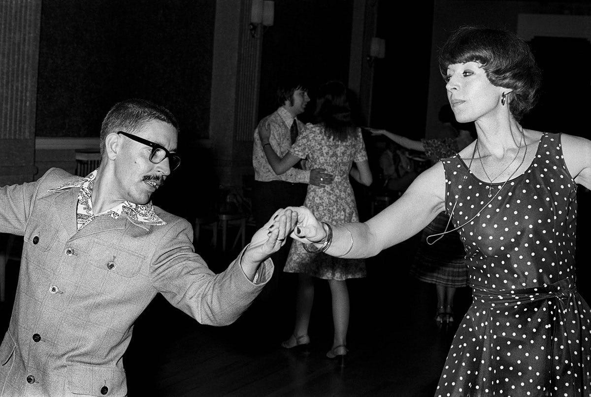Black and white photograph from Vulcan's Forge showing a person in a suit and glasses dancing with someone in a polka dot sleeveless dress