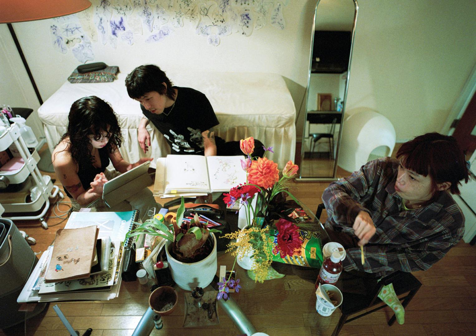 Photograph from Dazed and Ikea's zine showing three people sat around a table in in a bedroom turned tattoo studio