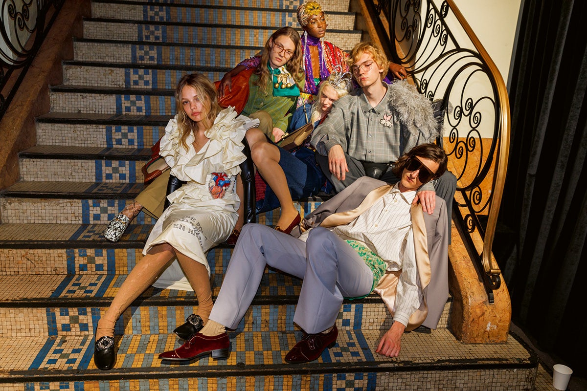 A group of six young people dressed in Gucci sitting in a heap on a tiled staircase photographed by Martin Parr
