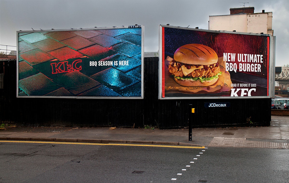 Two KFC billboards, one showing the brand's logo reflected in a puddle, the other showing its new Ultimate BBQ Burger
