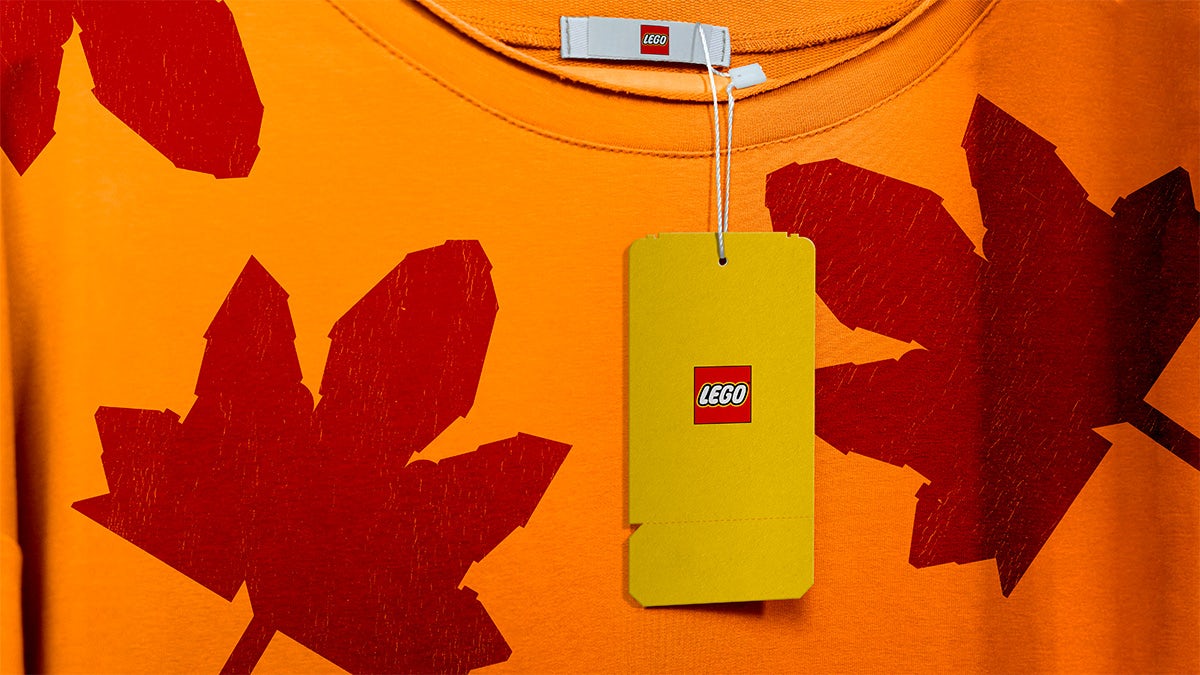 Image shows a yellow Lego clothing tag attached to an orange T-shirt covered in red maple leaf patterns