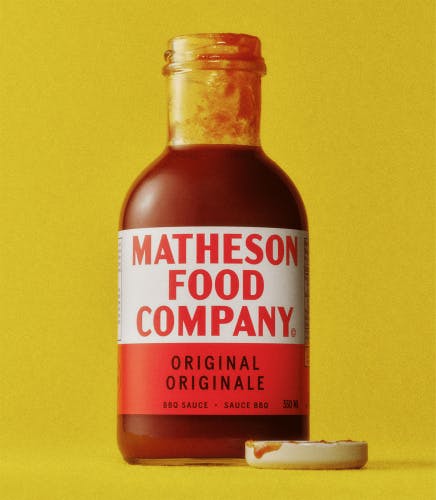 Image showing a corked sauce bottle featuring a red and white label, shown against a yellow background, created as part of the branding for Matheson Food Company