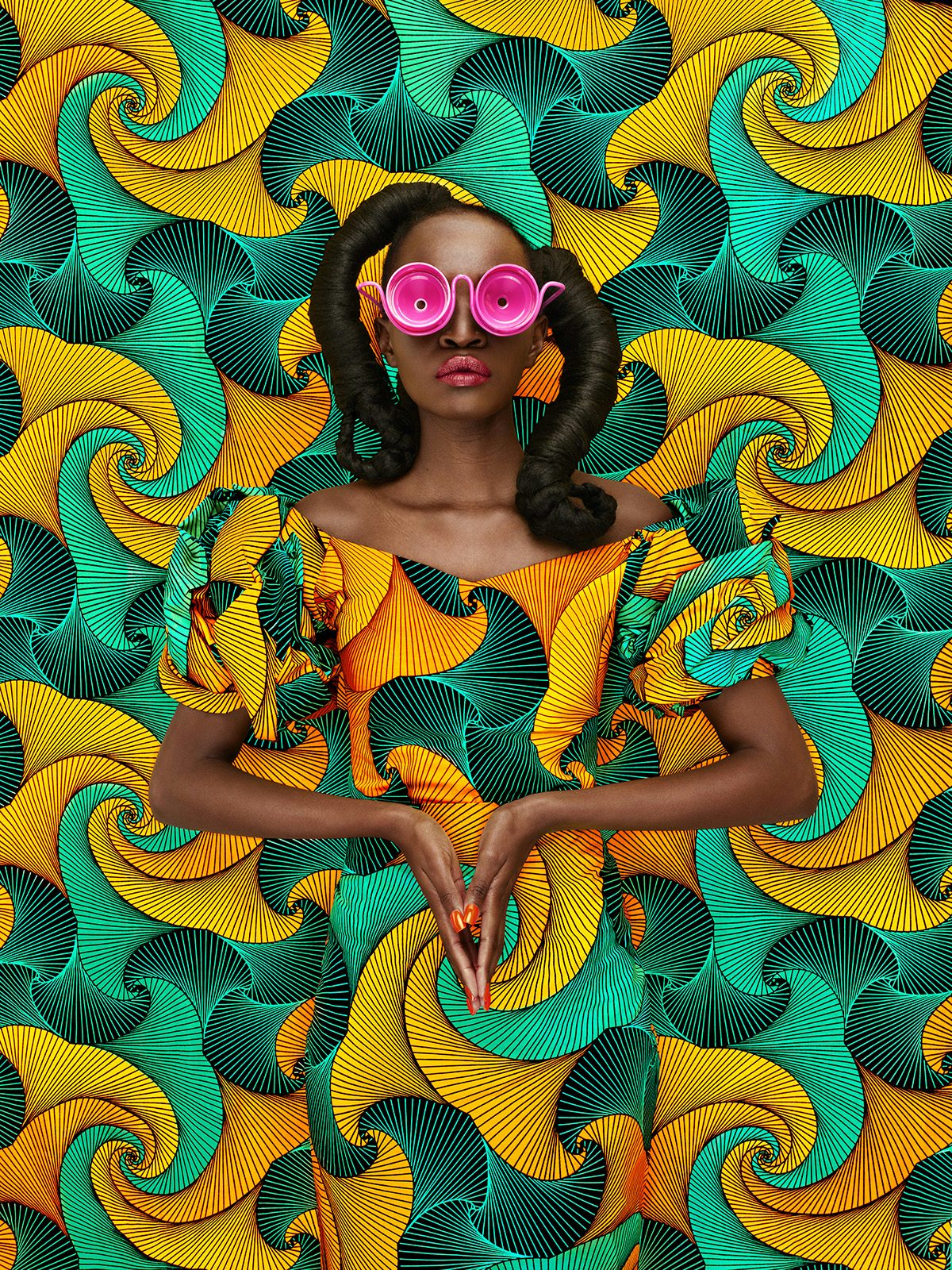 A woman wearing a pink glasses and a garment in a yellow and green swirling pattern, which blends into a backdrop in the same pattern