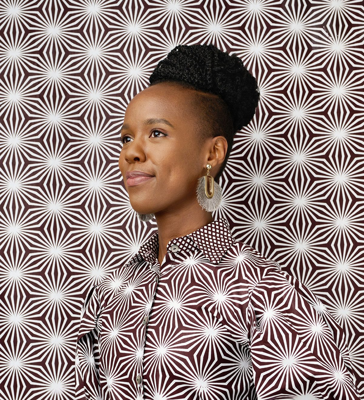 A woman wearing a garment in a maroon and white starburst pattern, which blends into a backdrop in the same pattern